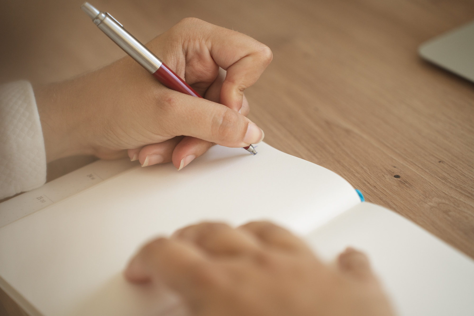 Texterin mit Gefuehl - Storytelling Leistung Storytelling. Am Foto: Eine Hand schreibt mit einem roten Kugelschreiber in ein Notizbuch.