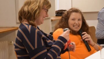 Die Autorin lächelt und hält eine Rose aus Eisen in der Hand und Julia Hofmarcher hält ein Mikrophon in der Hand und lächelt.