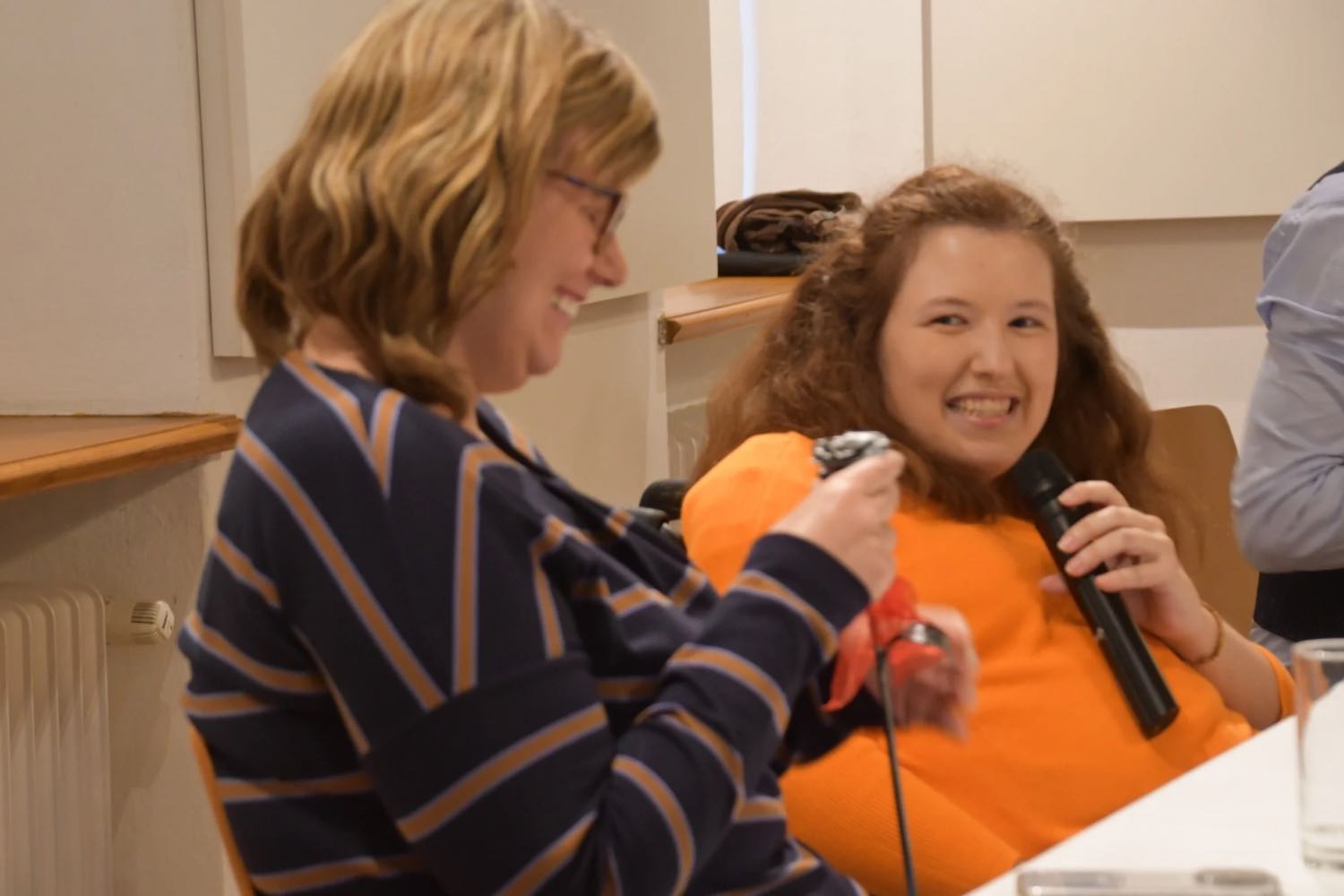 Die Autorin lächelt und hält eine Rose aus Eisen in der Hand und Julia Hofmarcher hält ein Mikrophon in der Hand und lächelt.