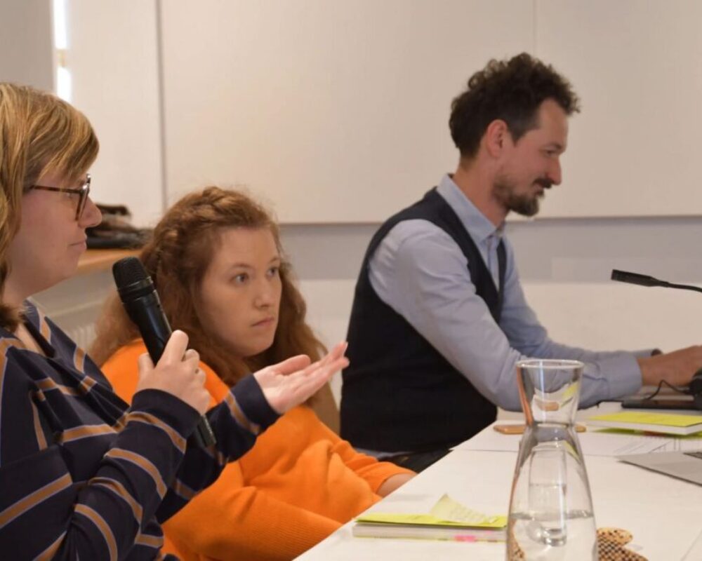 Am Tisch sitzen in einer Reihe Hannah Wahl (ein Mikrophon in der Hand), Julia Hofmarcher und ihr Bruder, Joseph.