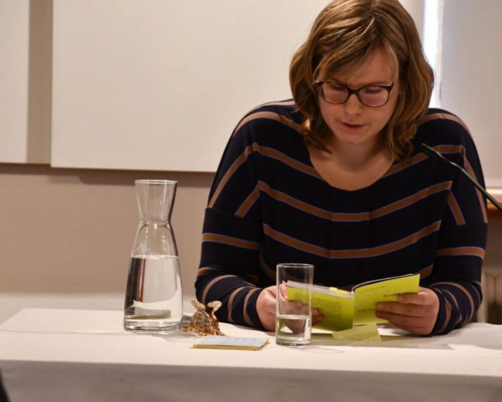 Hannah Wahl sitzt am Tisch und liest aus ihrem Buch vor.